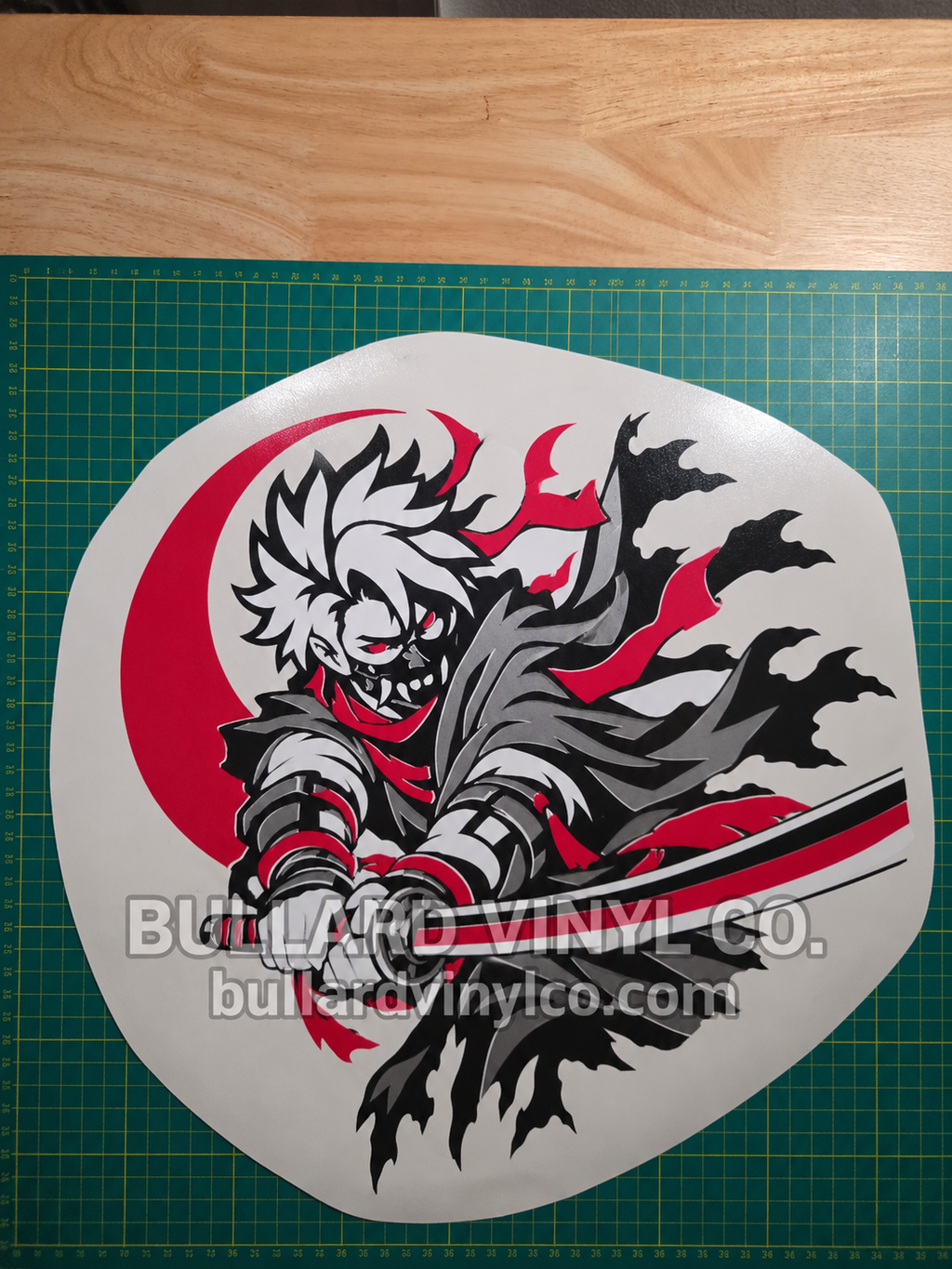 Actual finished Crimson Ronin layered vinyl decal shown upright on its release liner over a cutting mat. Bullard Vinyl Co. watermark is not part of the decal.